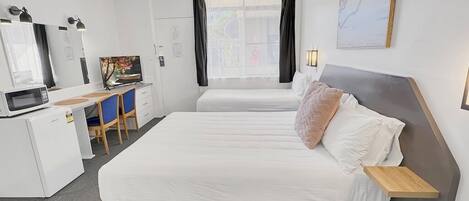 A hotel room with a bed, desk, chair, TV, and a window with curtains.