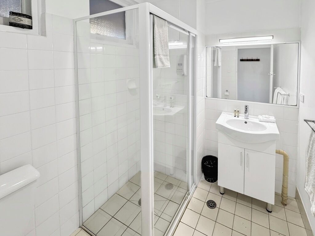 A modern bathroom with a glass-enclosed shower, a white sink, and a large mirror.
