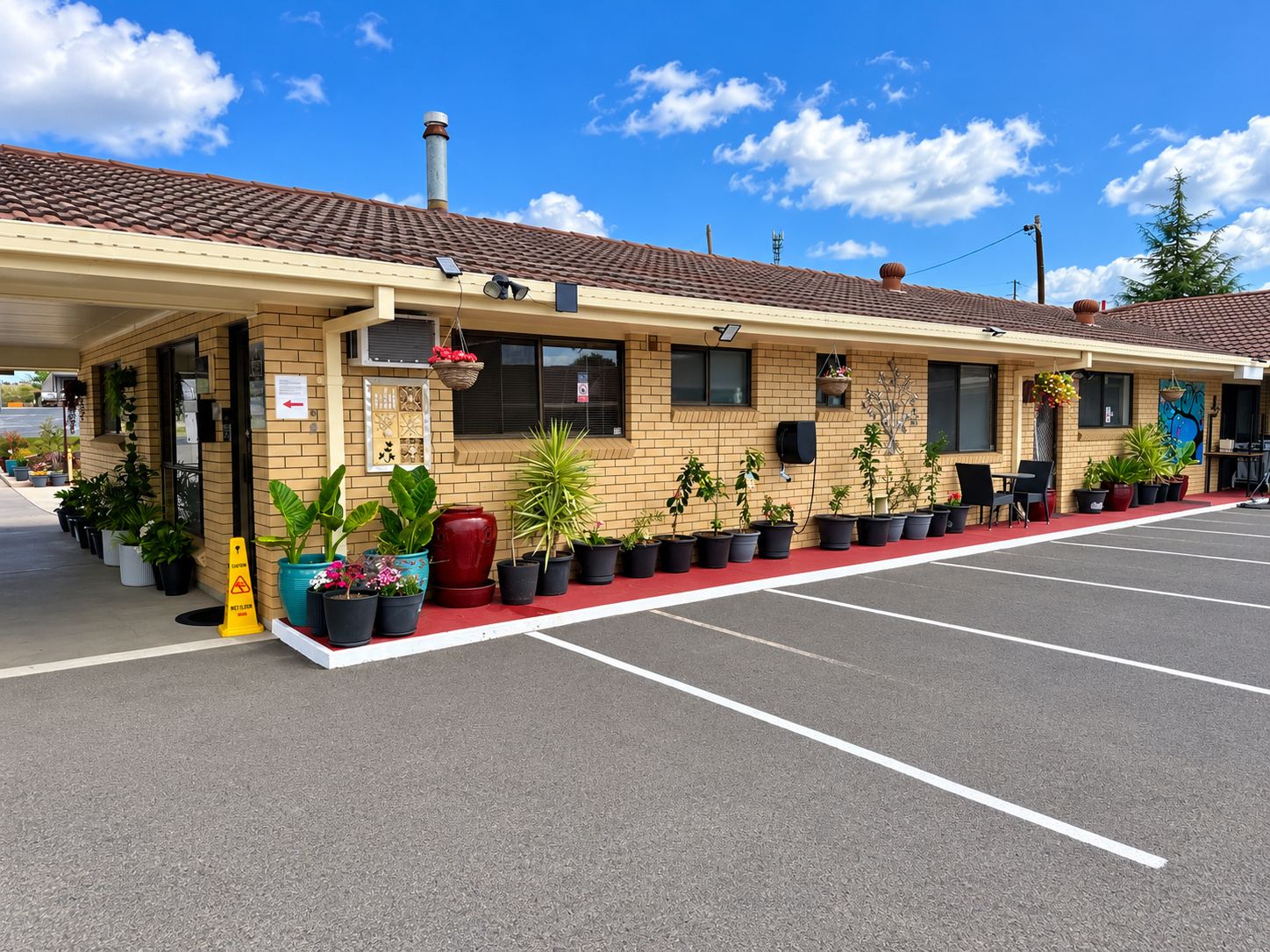 Un motel con zona de estacionamiento techada, plantas en macetas y cielo despejado.