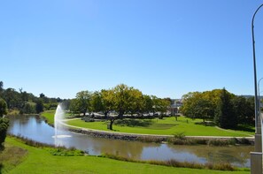 Escape to a serene park setting with a peaceful body of water, fountain, and lush greenery.