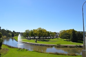 Escape to a serene park setting with a peaceful body of water, fountain, and lush greenery.
