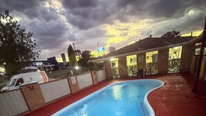A swimming pool with a red deck, surrounded by a brick wall and a fence. - Top Of The Town Motel (Inverell)