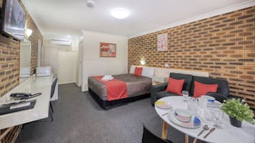 Une chambre d’hôtel compacte comprenant un lit, un canapé, un bureau avec un téléphone et une table à manger mise avec des assiettes, des verres et une plante.