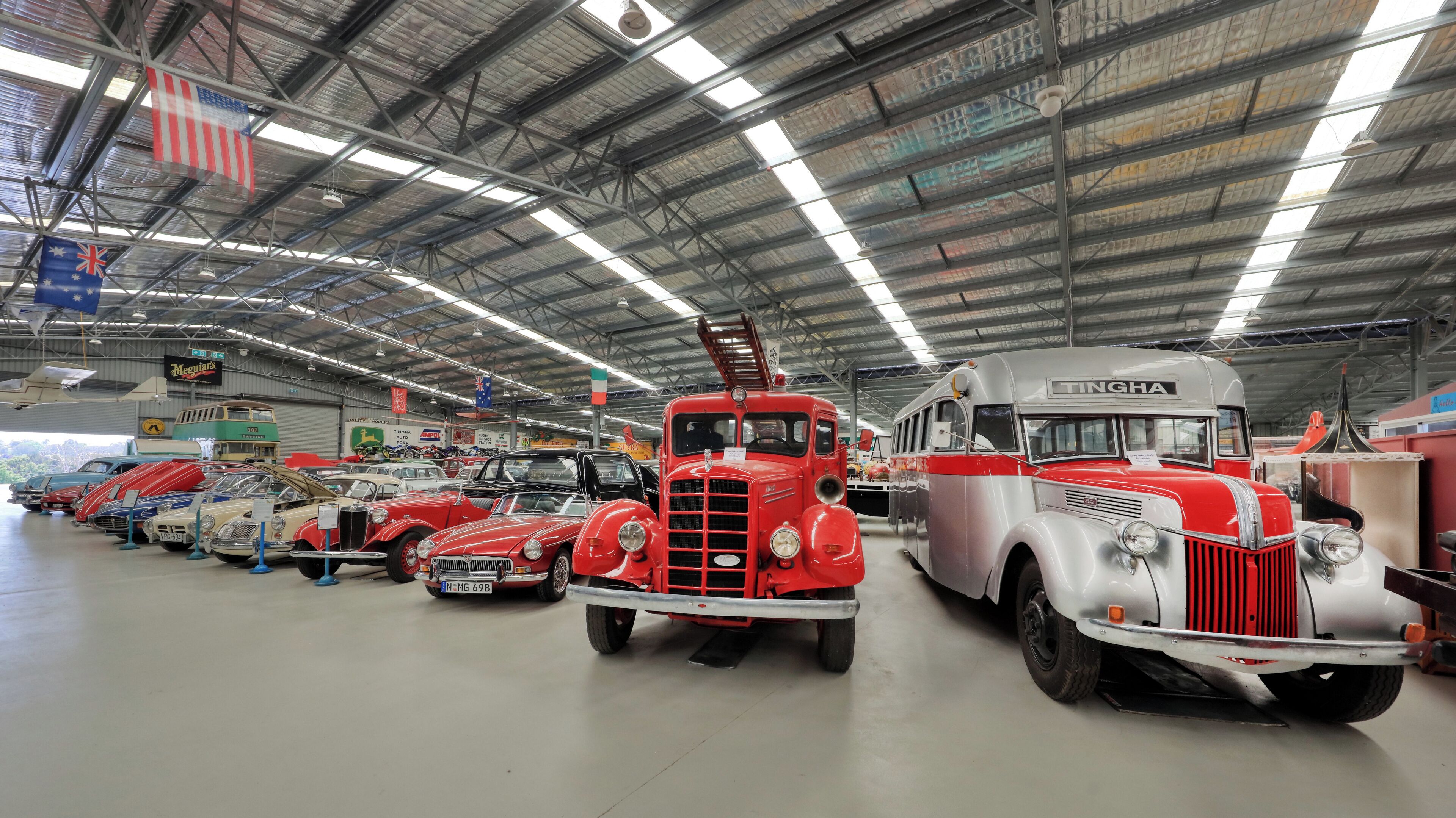 A large indoor exhibition hall with vintage vehicles on display, including a prominent red truck and a silver bus.