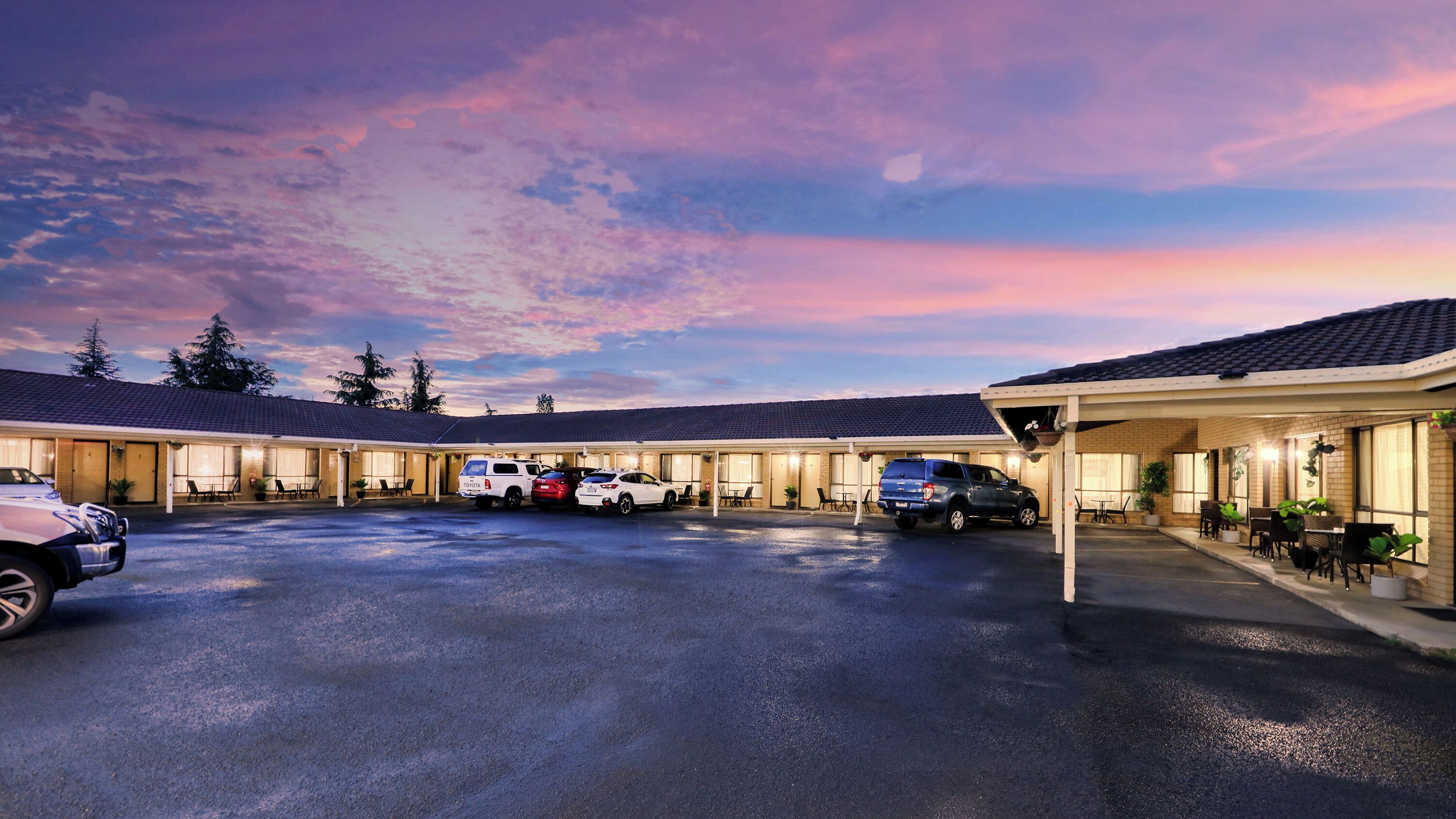 Un motel con estacionamiento techado, varias habitaciones y vistas del cielo al atardecer.
