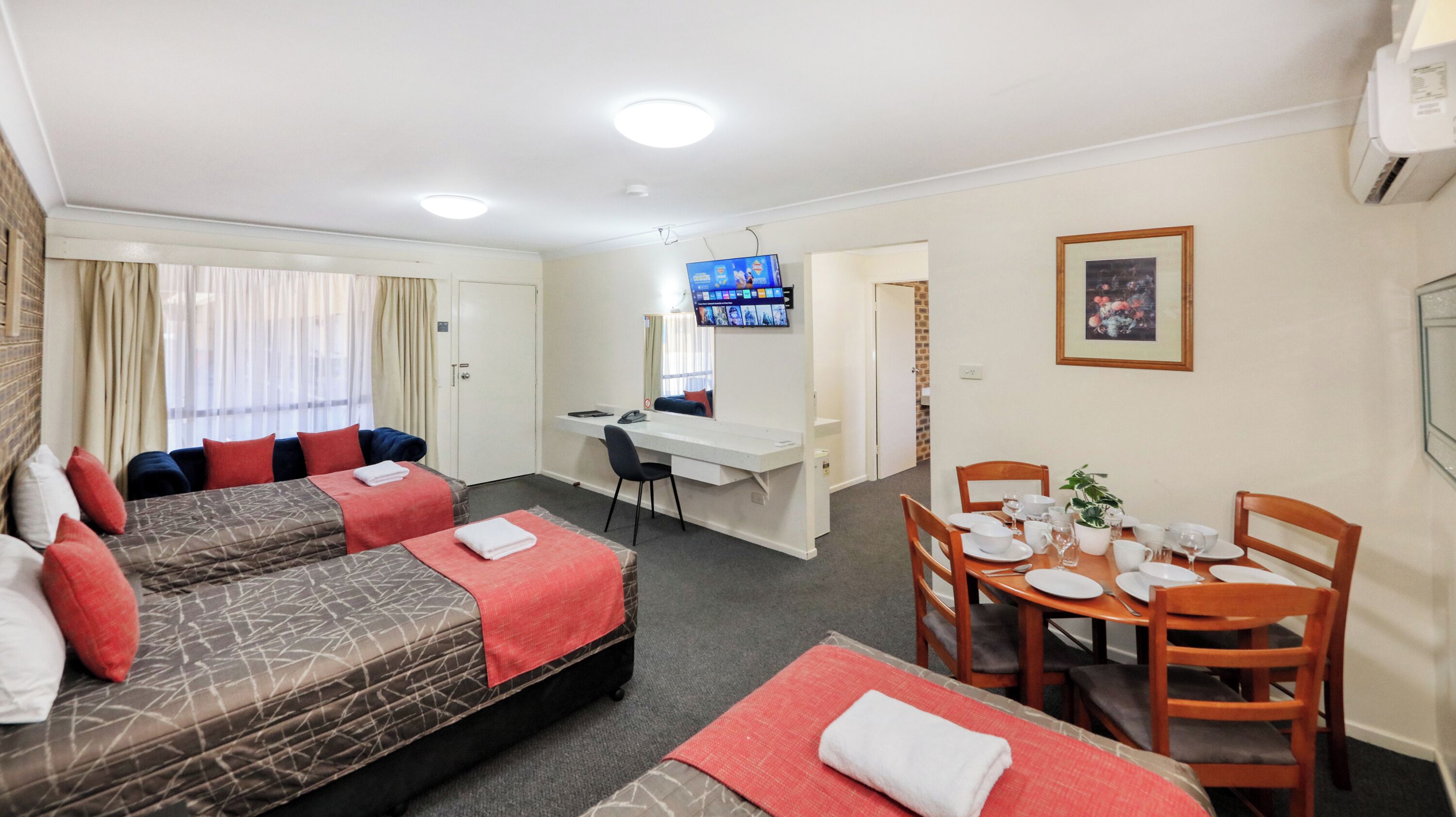 Habitación de hotel con dos camas, un escritorio, una mesa de comedor y una televisión.
