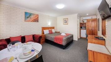 A compact hotel room with a bed, a small desk, a dining table with chairs, and a kitchenette.