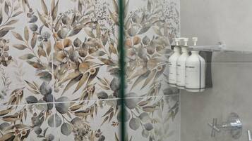 A bathroom with a floral wallpaper design, a shower area, and a shelf with toiletries.