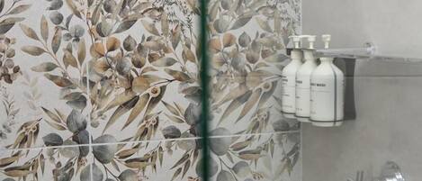Un baño con diseño de papel tapiz floral, una zona de ducha y un estante con artículos de aseo.