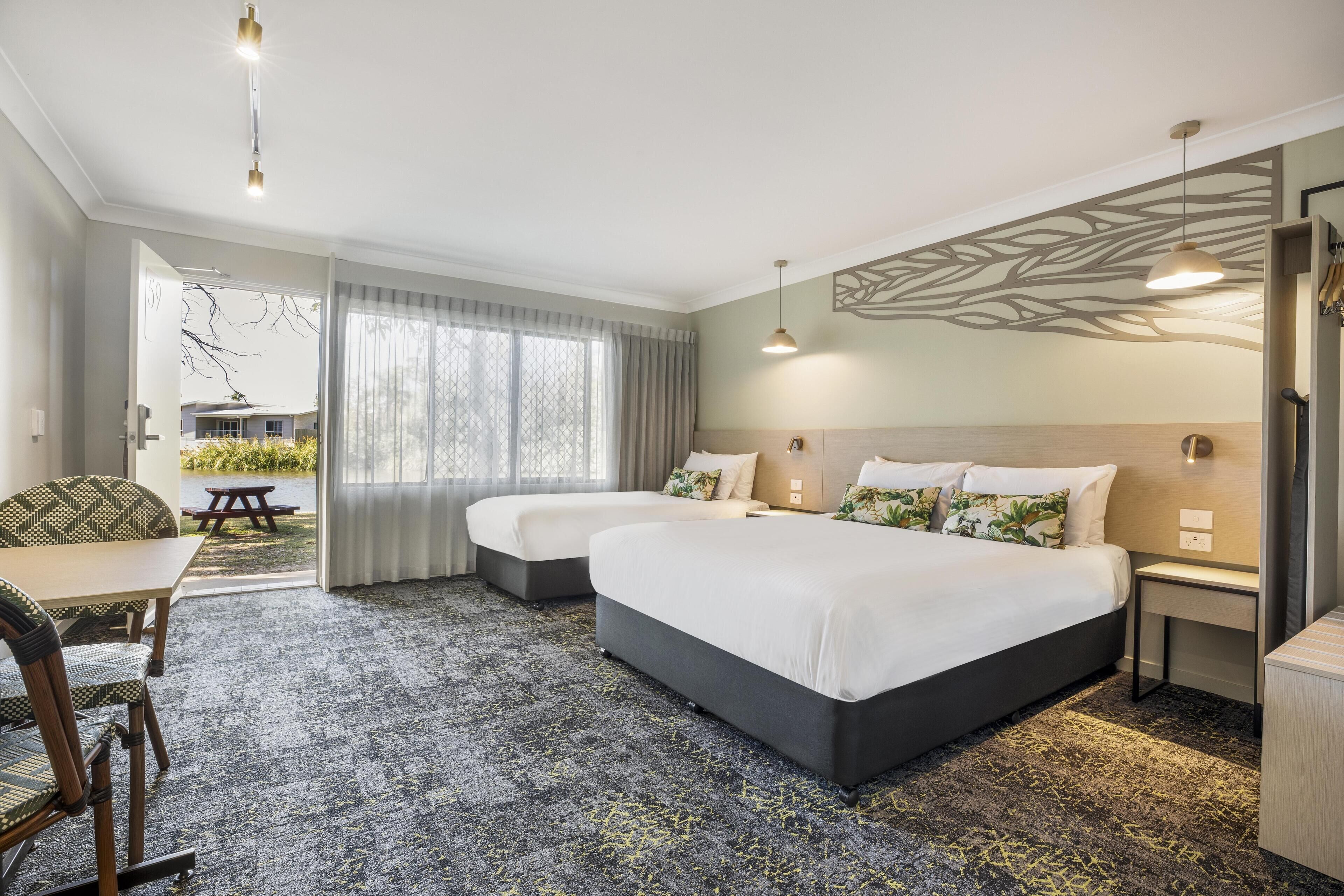 A hotel room with two beds, a dining table, and a view of the outdoors.