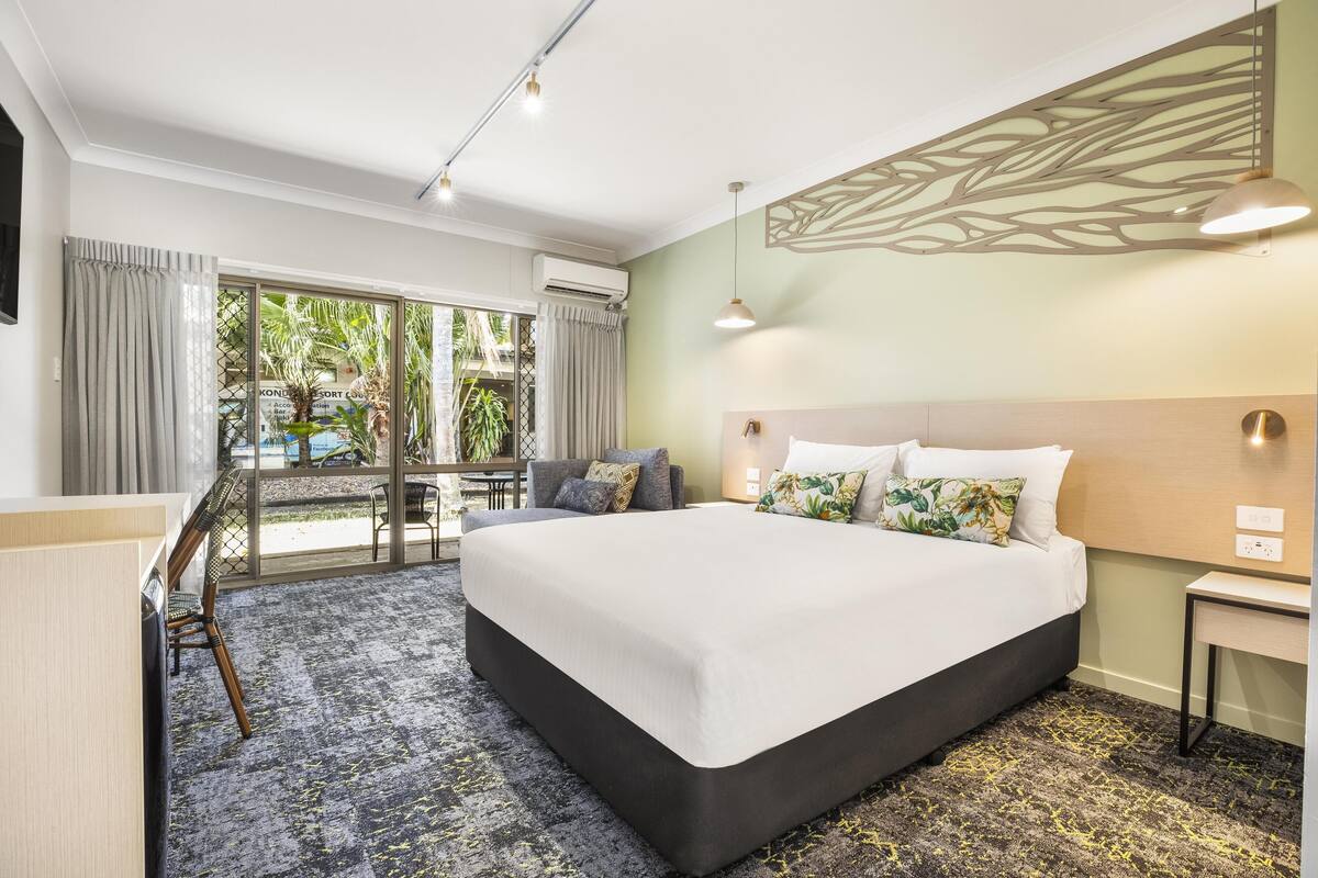 A hotel room with a large bed, a desk, a chair, and a view of the outdoors.