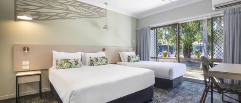 A hotel room with two beds, a small table, a chair, and a view of the outdoors.