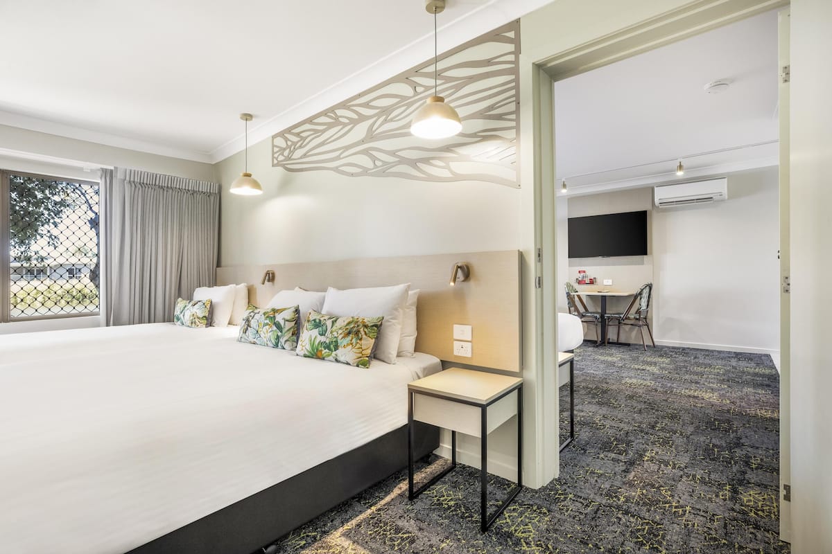 A hotel room with a large bed, a desk, a TV, and a patterned carpet.