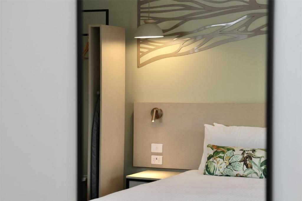 A hotel room with a bed, a nightstand, a wall-mounted lamp, and a decorative wall piece.