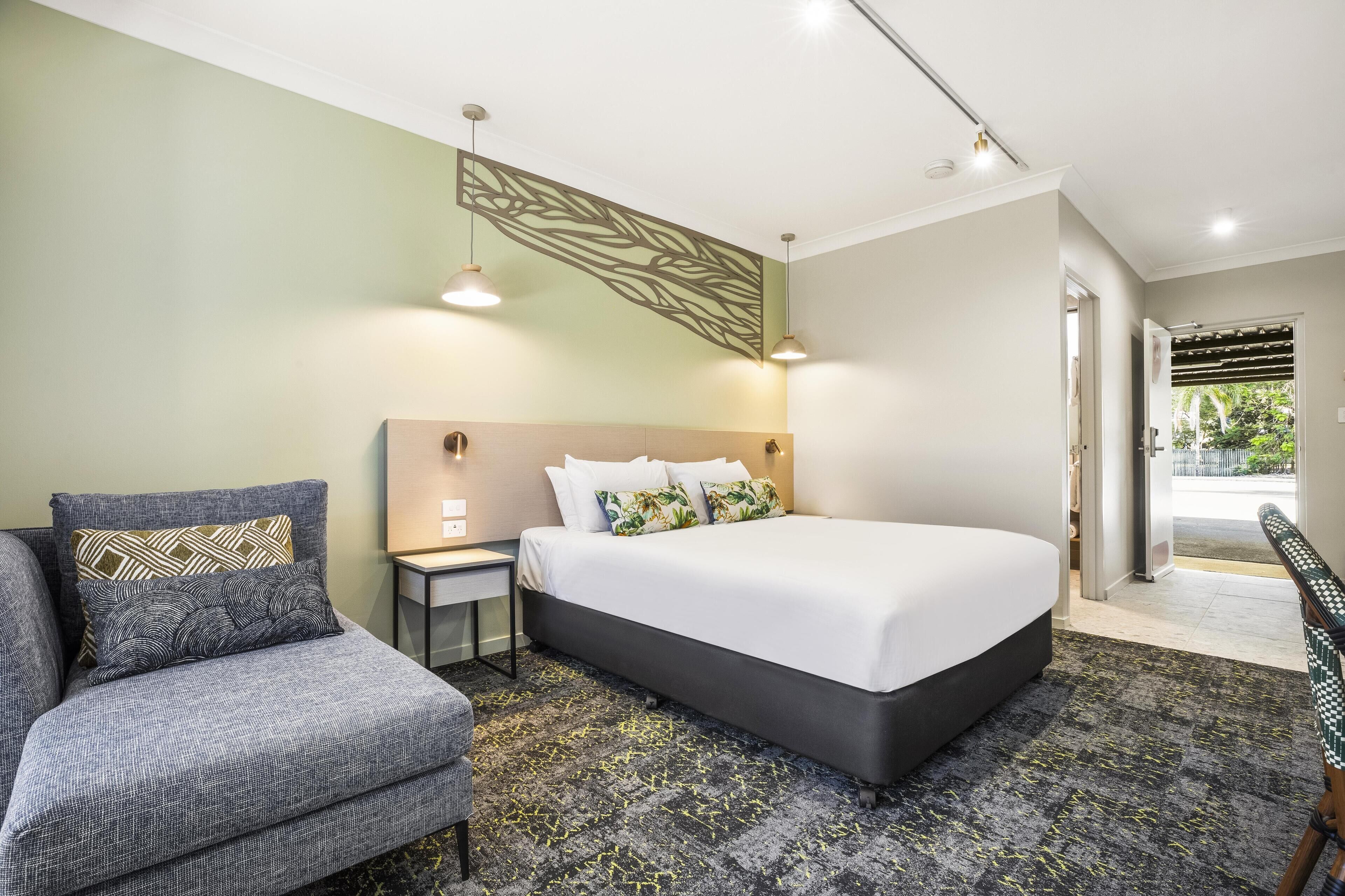 A modern hotel room with a large bed, a sofa, a nightstand, and a decorative wall panel.