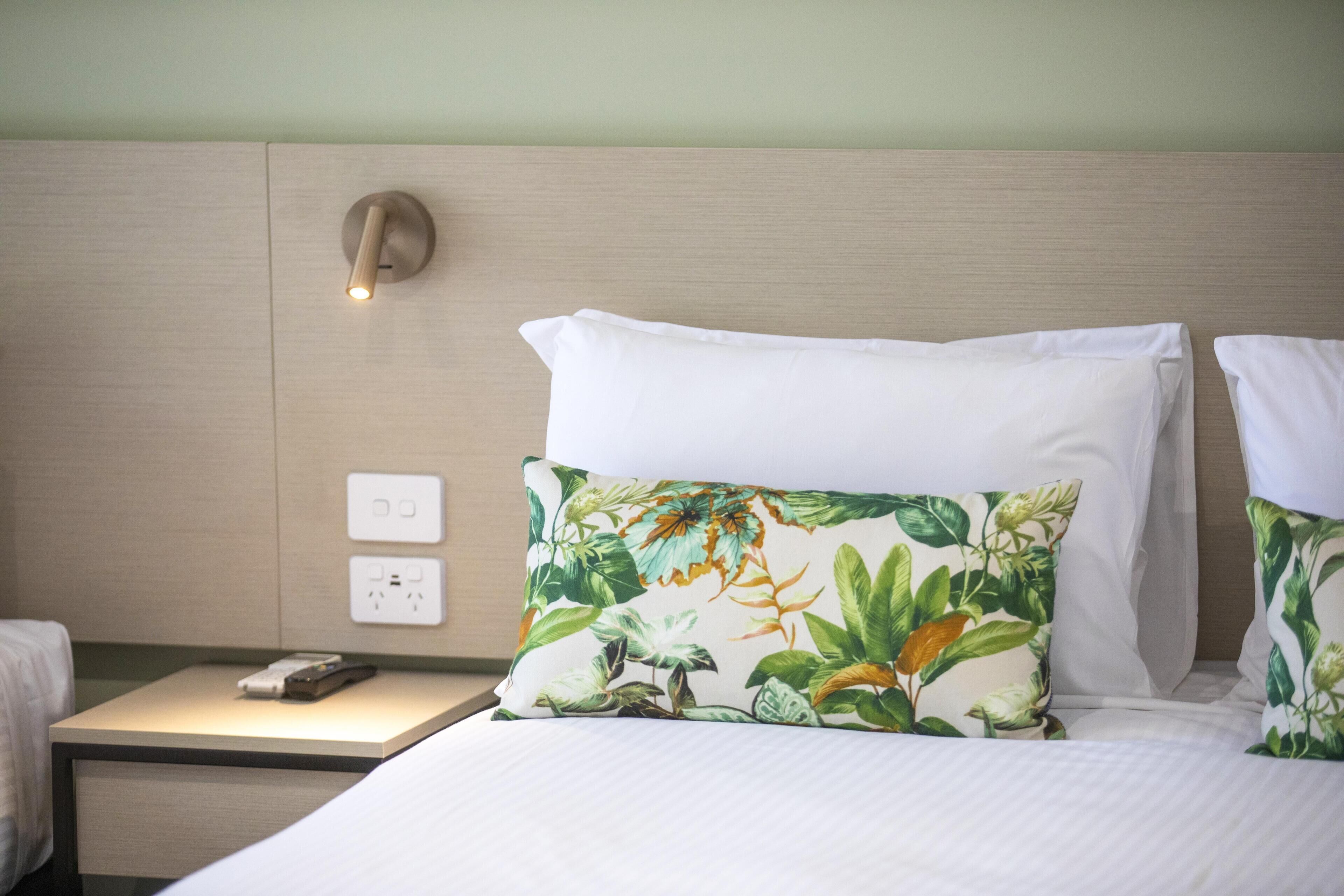 A hotel room with a bed, two pillows, a nightstand, a phone, and a wall socket.