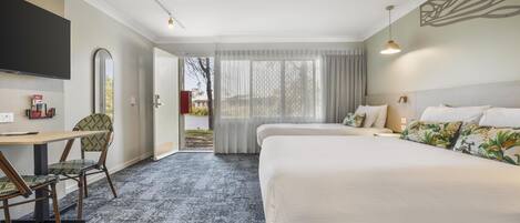 A hotel room with two beds, a desk with a chair, a TV, and a view of the outdoors.