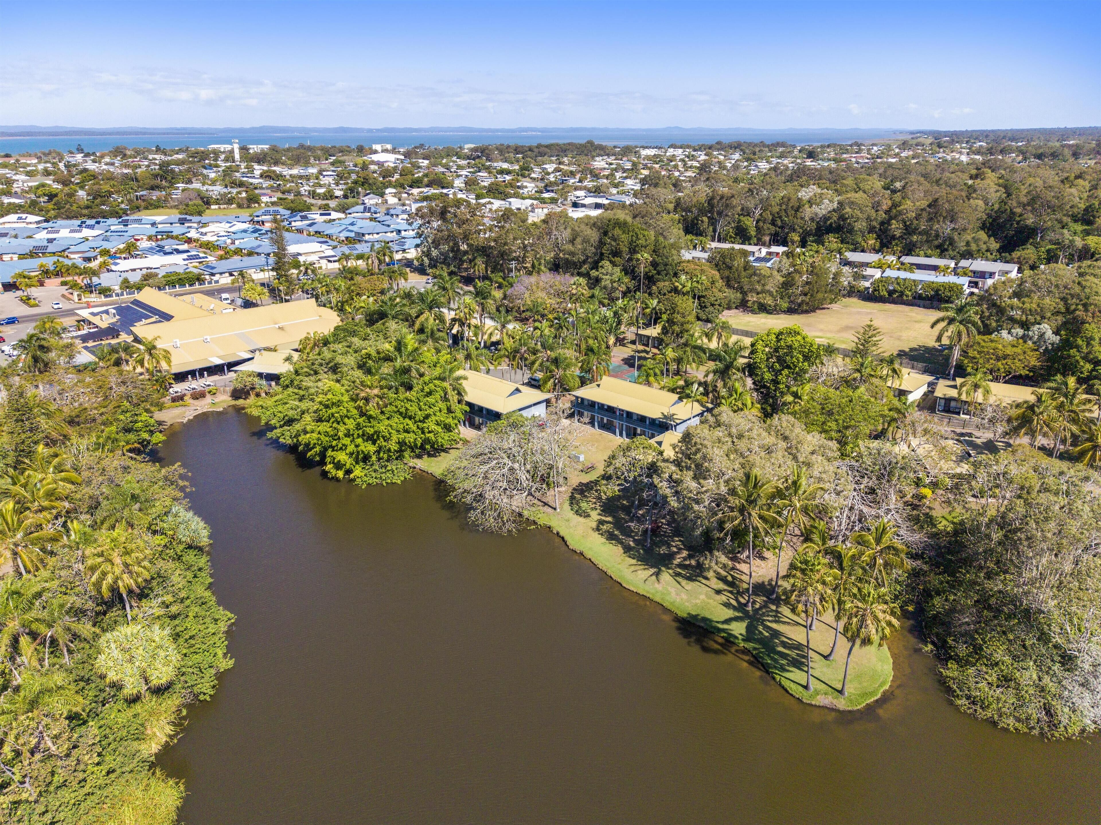 An aerial view of a residential area with houses, a river, and a distant coastline.