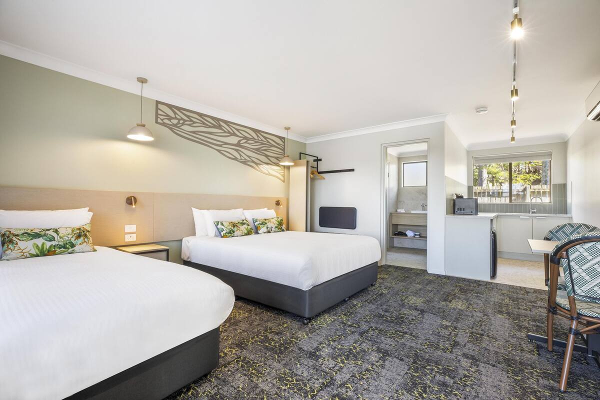 A hotel room with two beds, a desk, a chair, and a small kitchenette.