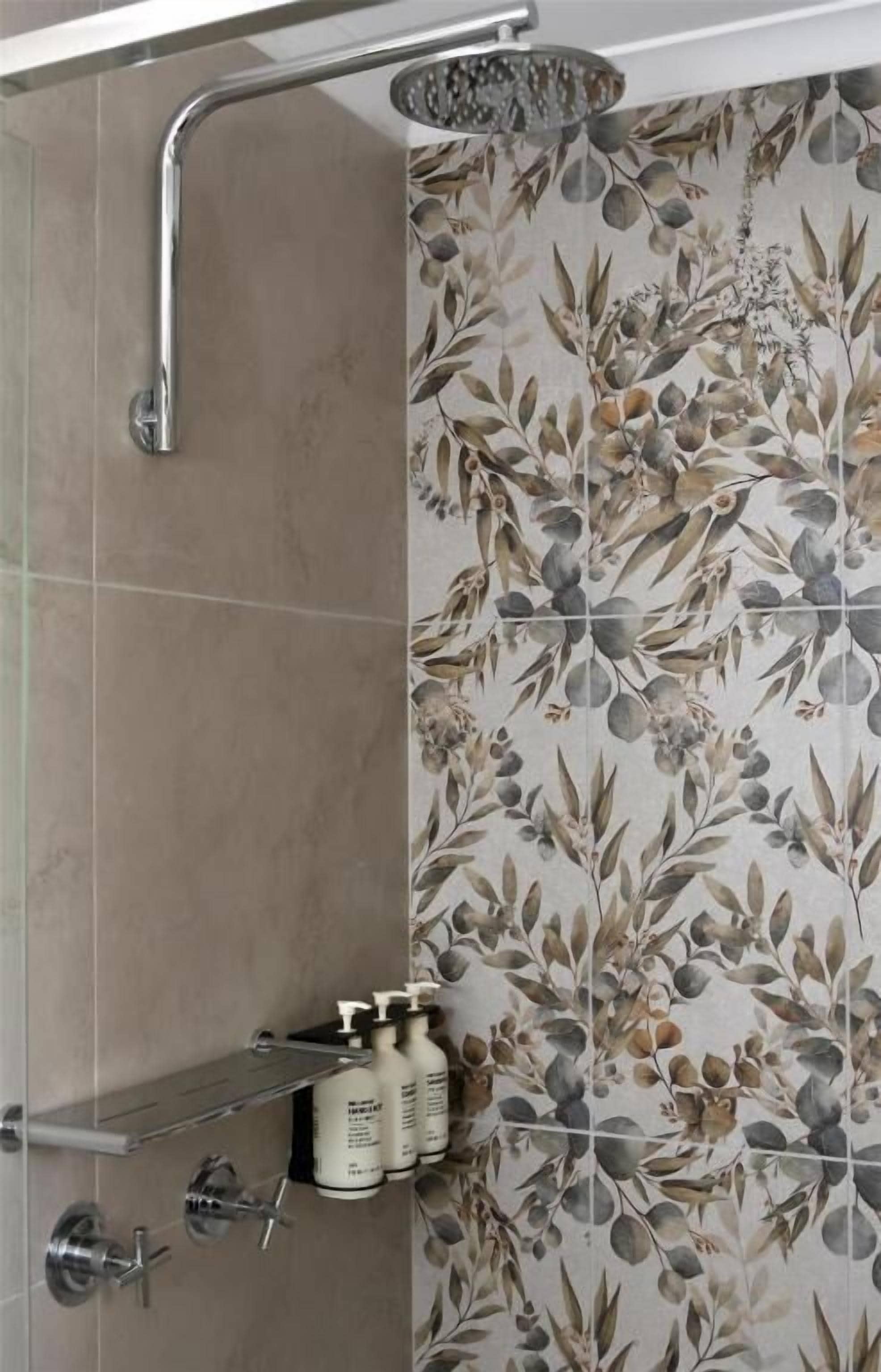 A shower area with a chrome faucet and showerhead, a shelf with toiletries, and a floral-patterned wall.