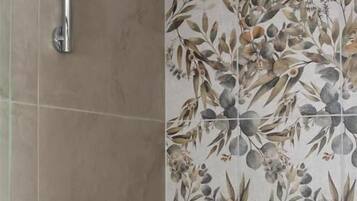 Un espace douche doté d’un robinet et d’une pomme de douche en chrome, d’une étagère pour les articles de toilette et d’un mur orné d’un motif floral.