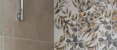 Un espacio de ducha con grifo y ducha de cromo, un estante con artículos de aseo y una pared con estampado floral.