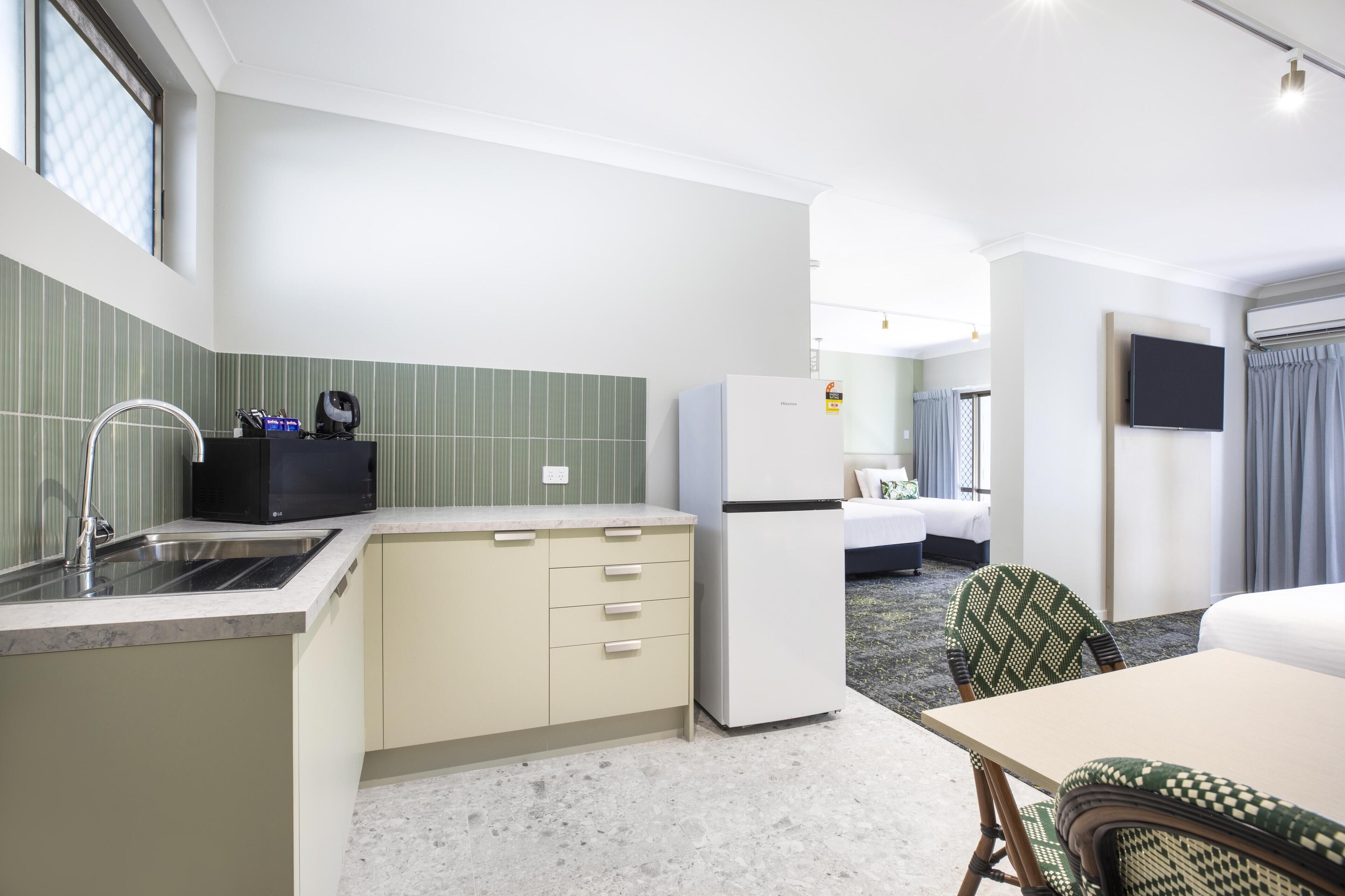 Une chambre d’hôtel de taille réduite, équipée d’une kitchenette, d’un lit, d’une télévision et d’une salle de bain.