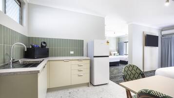 Una camera d'albergo compatta con angolo cottura, un letto, una TV e un bagno.