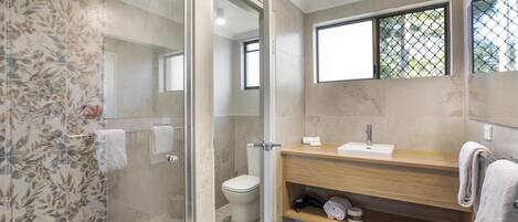 A modern bathroom with a glass-enclosed shower, a toilet, a wooden vanity with a sink, and a window with a view.
