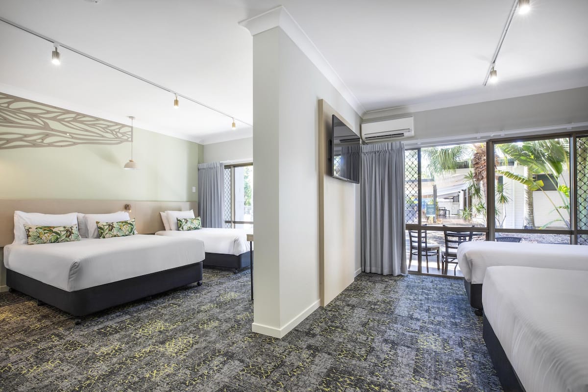 A hotel room with two beds, a large window with curtains, a flat-screen TV, and a ceiling fan.
