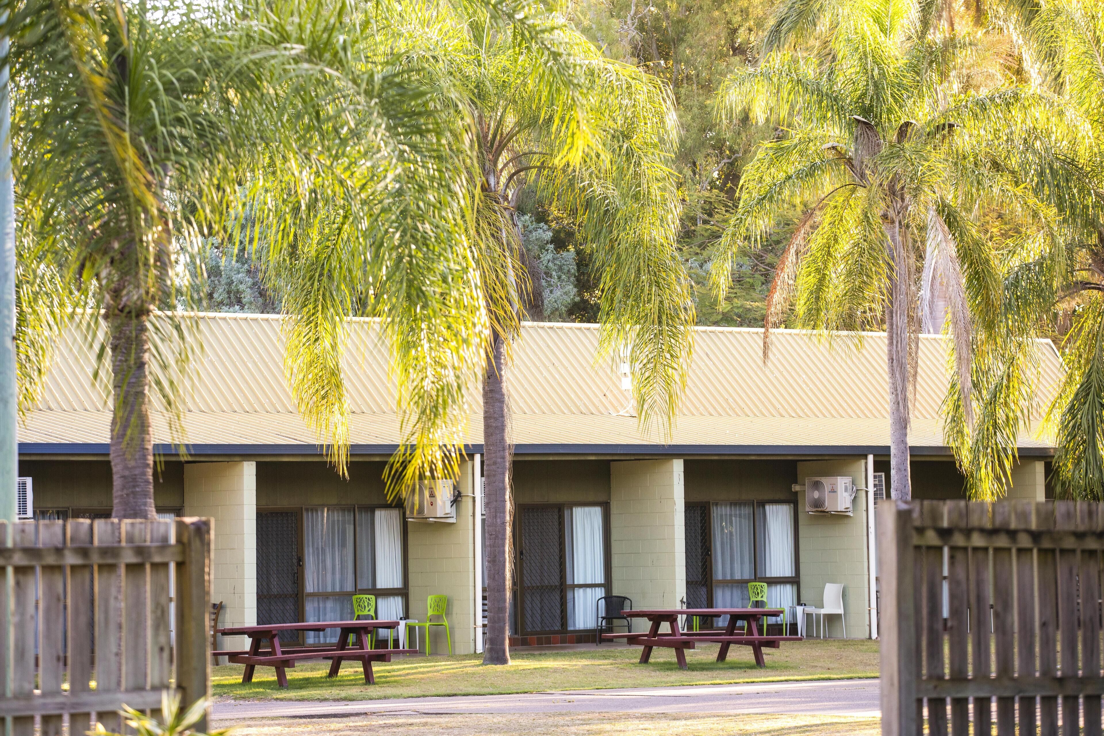 A motel with two picnic tables and chairs in front of a building with a corrugated metal roof.