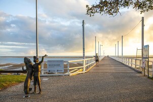 Um píer com uma placa, uma estátua e uma pessoa caminhando.