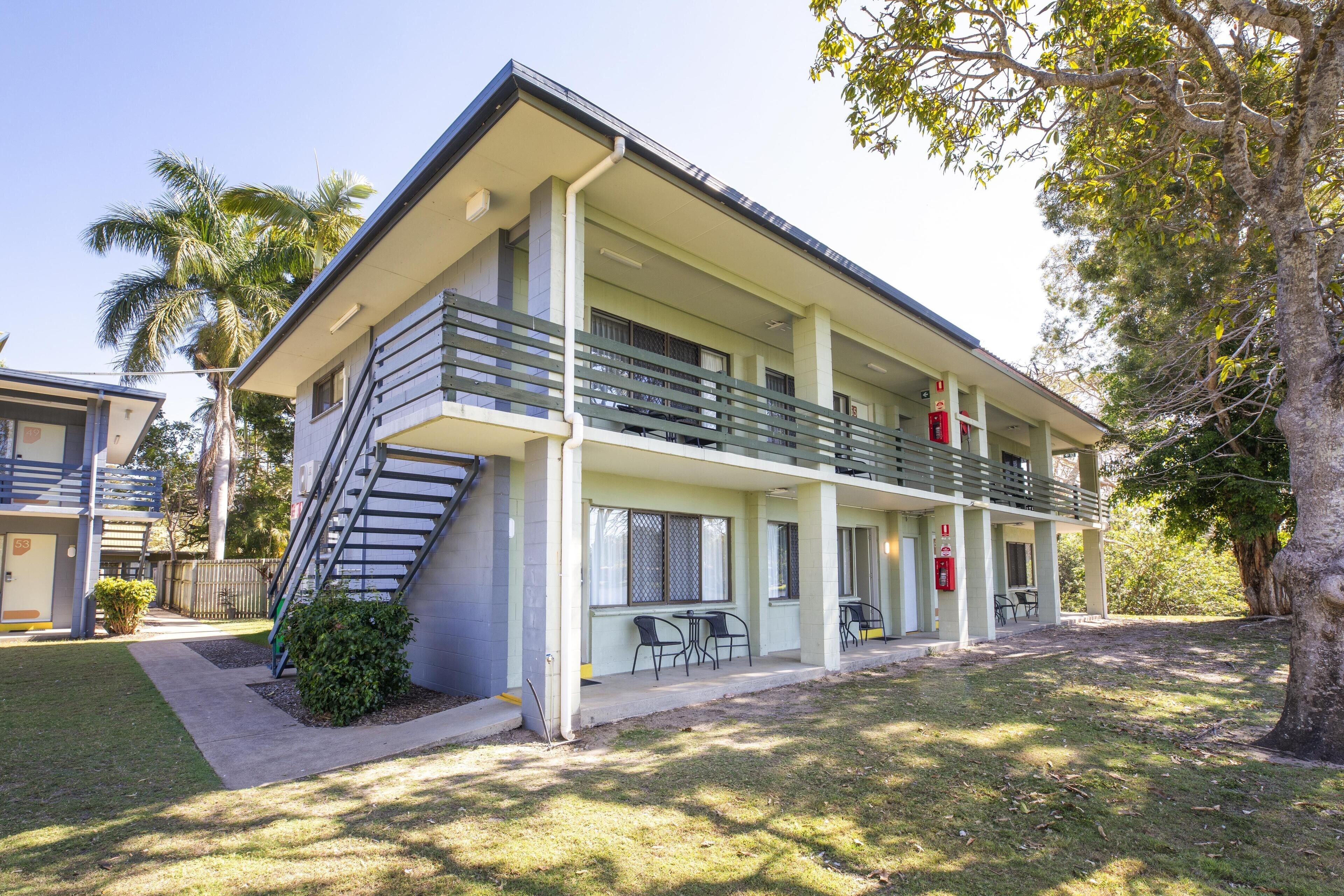 A two-story motel with a balcony on the second floor, a fire extinguisher, and a small outdoor seating area.