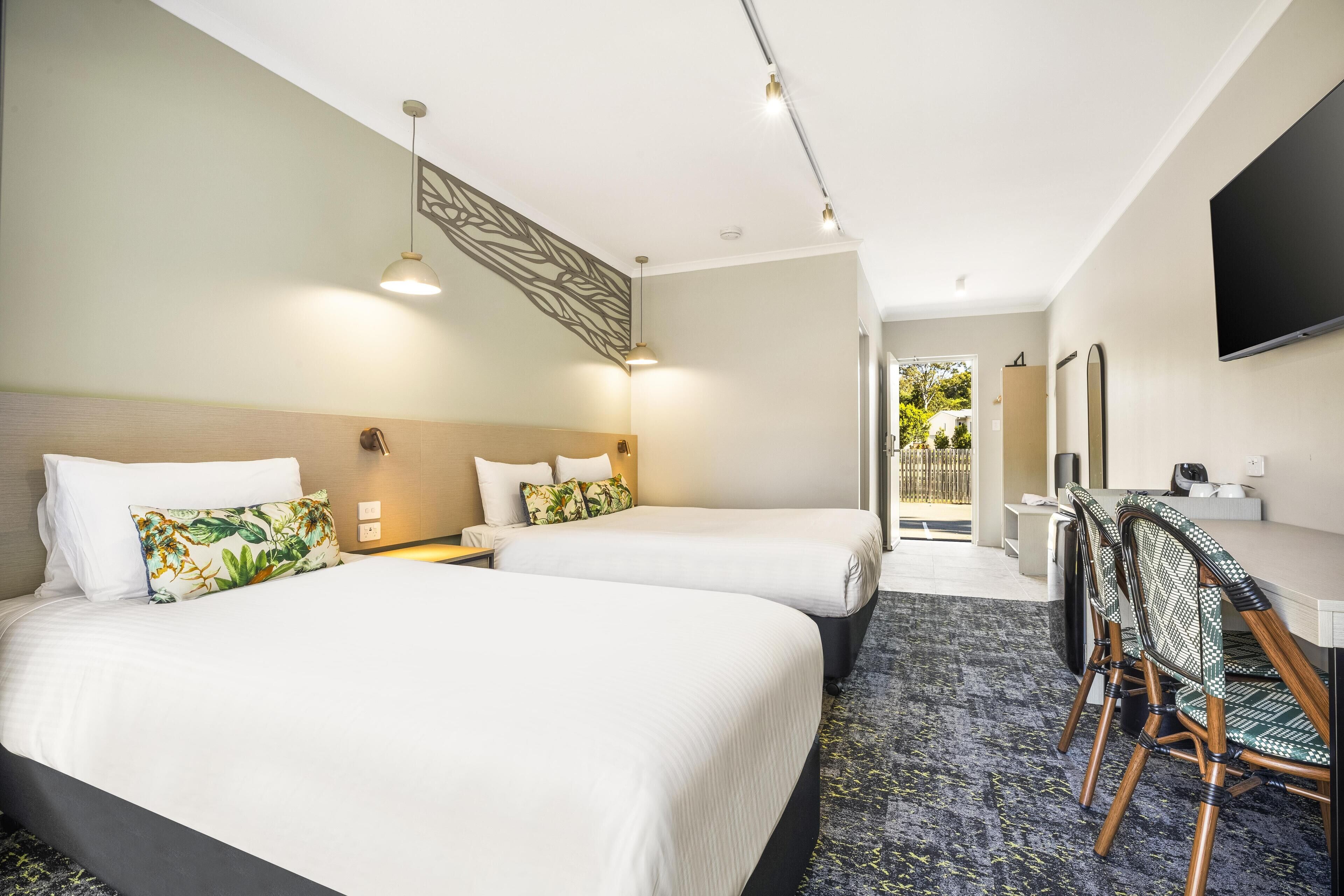 Habitación de hotel con dos camas, un escritorio con sillas, un televisor de pantalla plana y vistas al exterior.