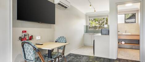 A modern room with a flat-screen TV, a small kitchenette, and a dining area with chairs and a table.