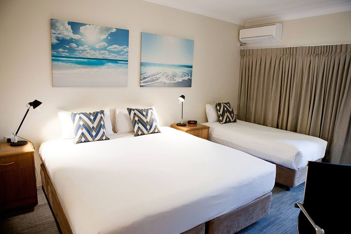 Habitación de hotel con dos camas, una mesita de noche con lámpara, un escritorio con lámpara y un equipo de aire acondicionado.