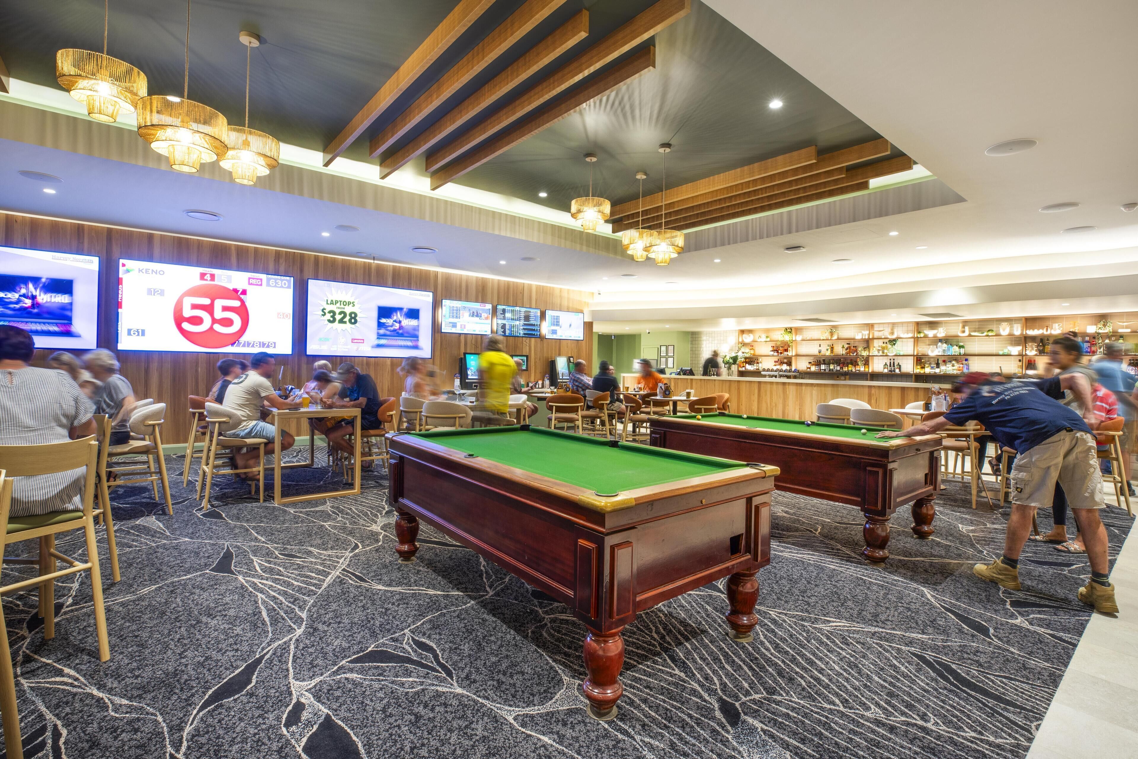 A pool hall with multiple pool tables, a bar area, and digital screens displaying promotions.