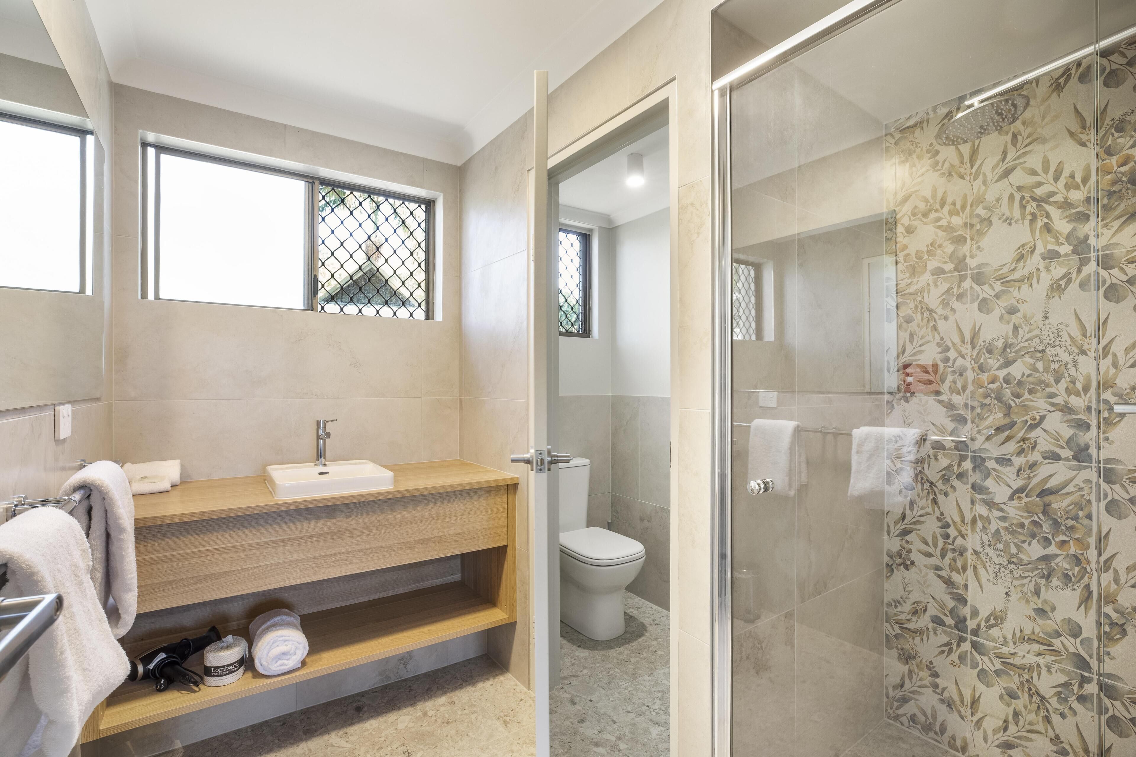 Un baño moderno con tocador de madera, inodoro y zona de ducha con mampara de vidrio.