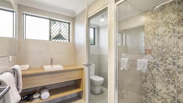 Un baño moderno con tocador de madera, inodoro y zona de ducha con mampara de vidrio.