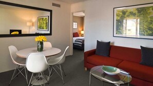 A modern hotel room with a dining area, a red sofa, and a large framed picture on the wall. -  Kingston Gardens Serviced Apartments  (Griffith)