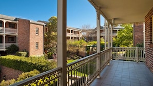A covered outdoor area with a tiled floor, surrounded by brick buildings with balconies and a garden area. -  Kingston Gardens Serviced Apartments  (Griffith)
