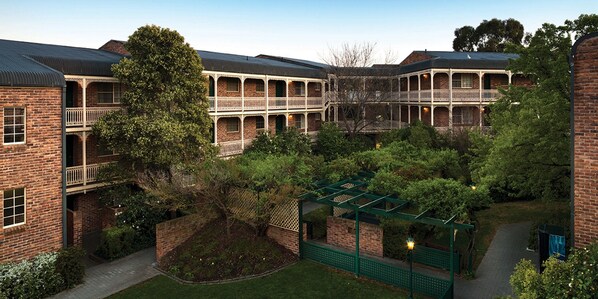 A courtyard with a brick building, a pergola, and a pathway. -  Kingston Gardens Serviced Apartments  (Griffith)
