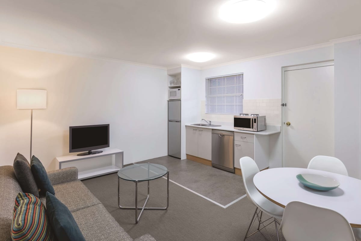 Eine moderne Wohnung mit Wohnzimmer, Küche und Essbereich. Sie verfügt über einen Flachbildfernseher, eine Mikrowelle, einen Kühlschrank und einen Esstisch mit Stühlen.