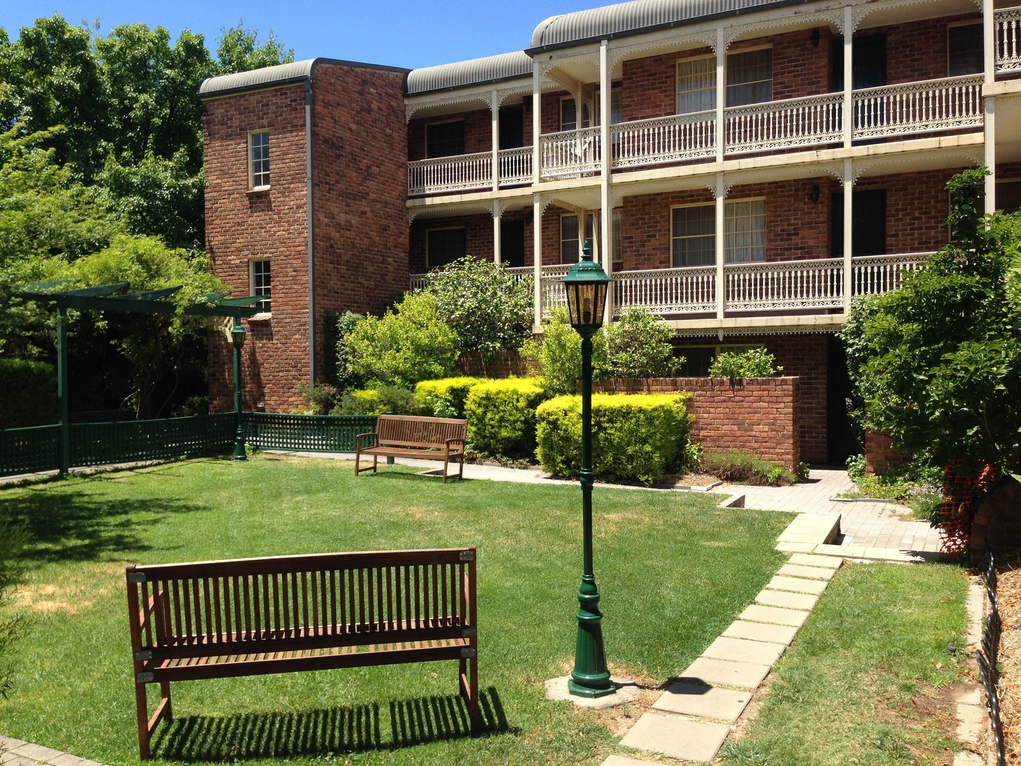 A brick building with a balcony, a bench, and a well-maintained lawn.