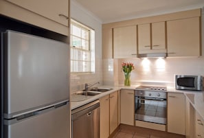 A modern kitchen with stainless steel appliances, a built-in oven, and a microwave. -  Kingston Gardens Serviced Apartments  (Griffith)