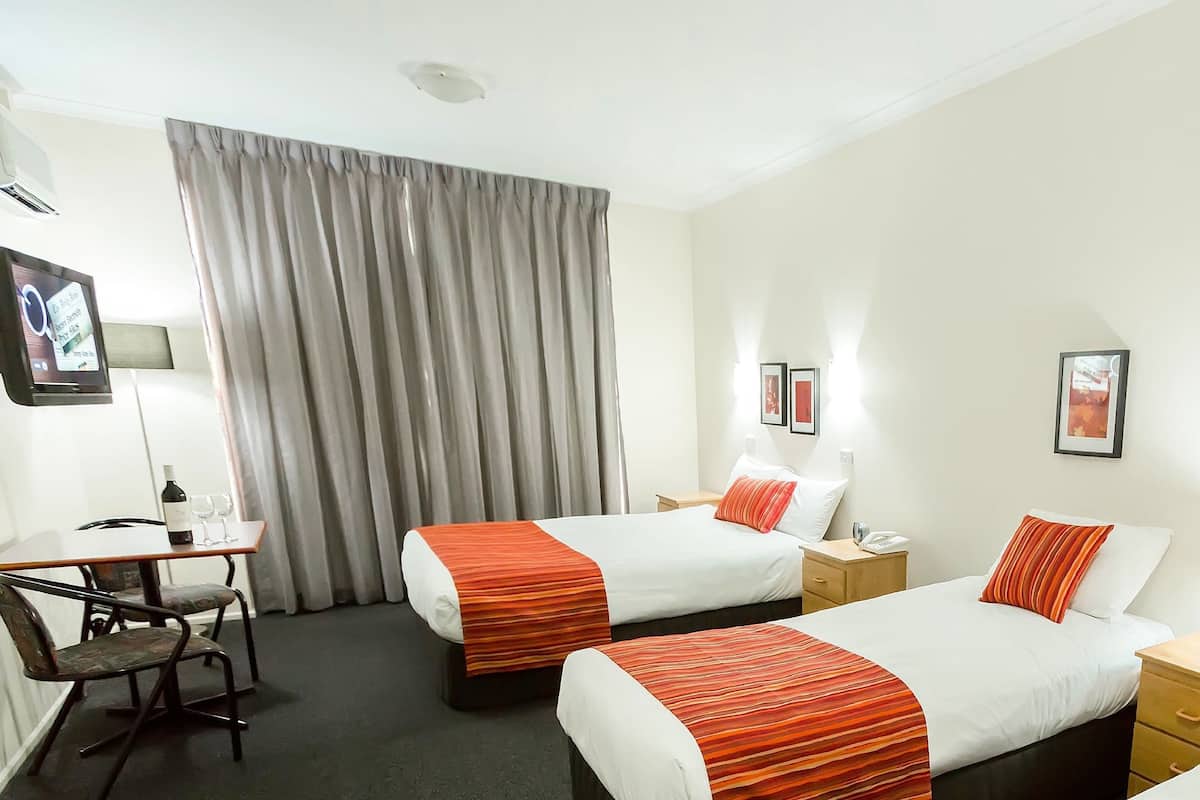 A hotel room with two beds, a desk, chairs, a TV, and a window with curtains.