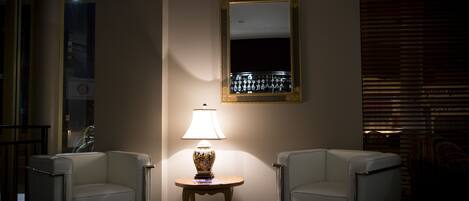Una habitación con dos sillones blancos, una mesita con lámpara y un espejo grande en la pared.