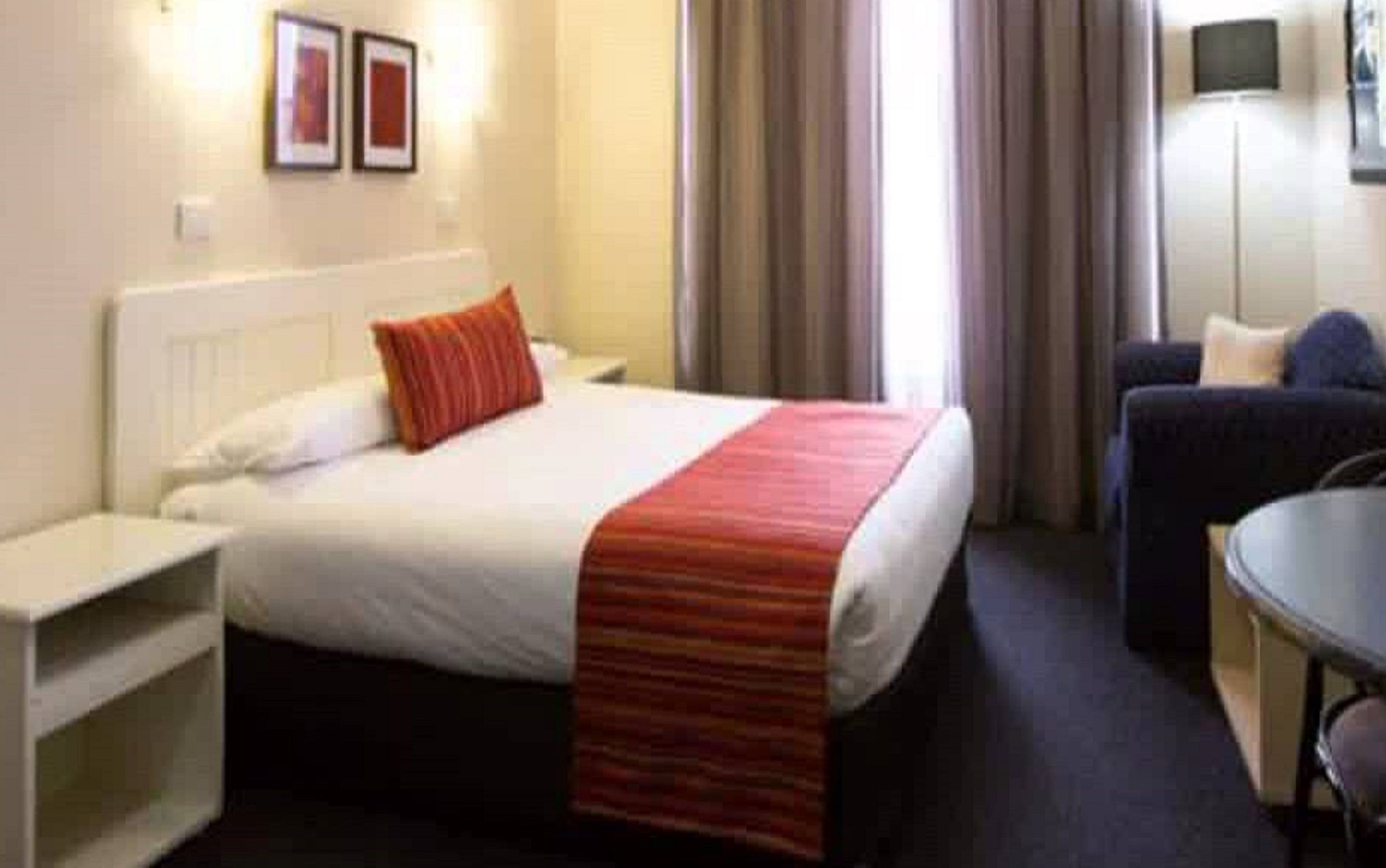 Une chambre d’hôtel avec un lit, un bureau, une chaise et un téléviseur fixé au mur.