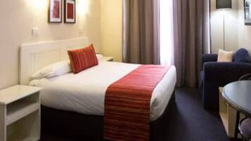 Une chambre d’hôtel avec un lit, un bureau, une chaise et un téléviseur fixé au mur.