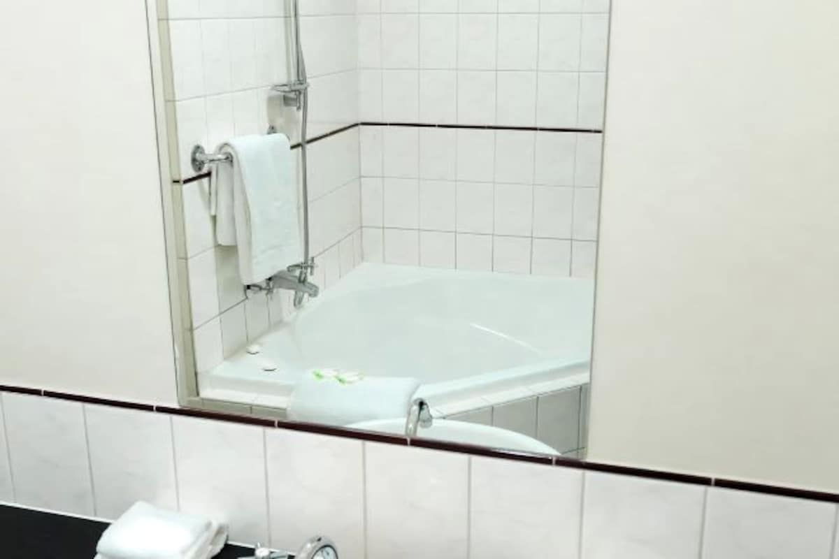 A modern bathroom with a glass-enclosed bathtub, white tiles, and a black countertop.